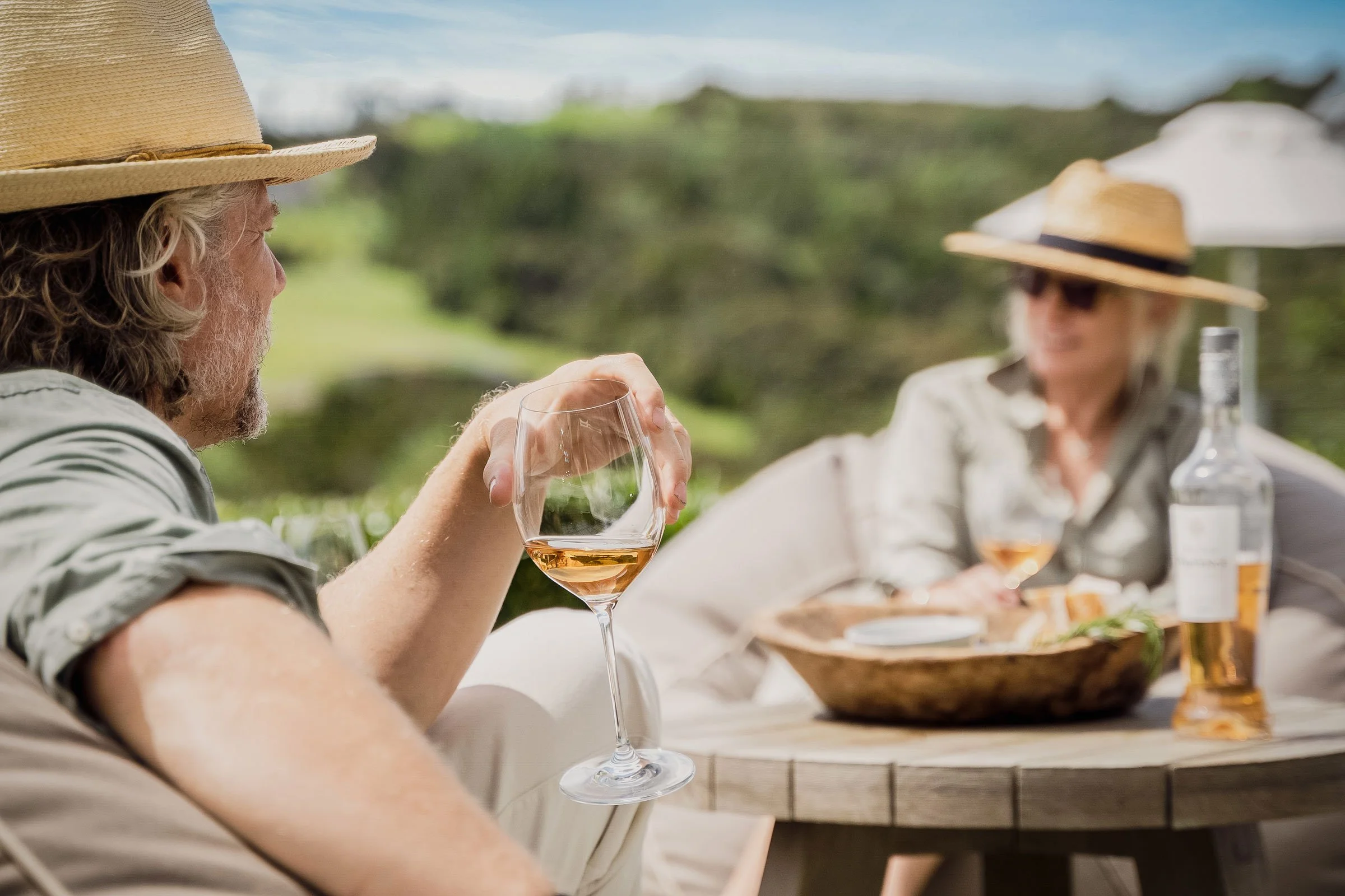 Two guests in straw hats sharing rosé and a grazing board on the lawn at Bluestone Estate.