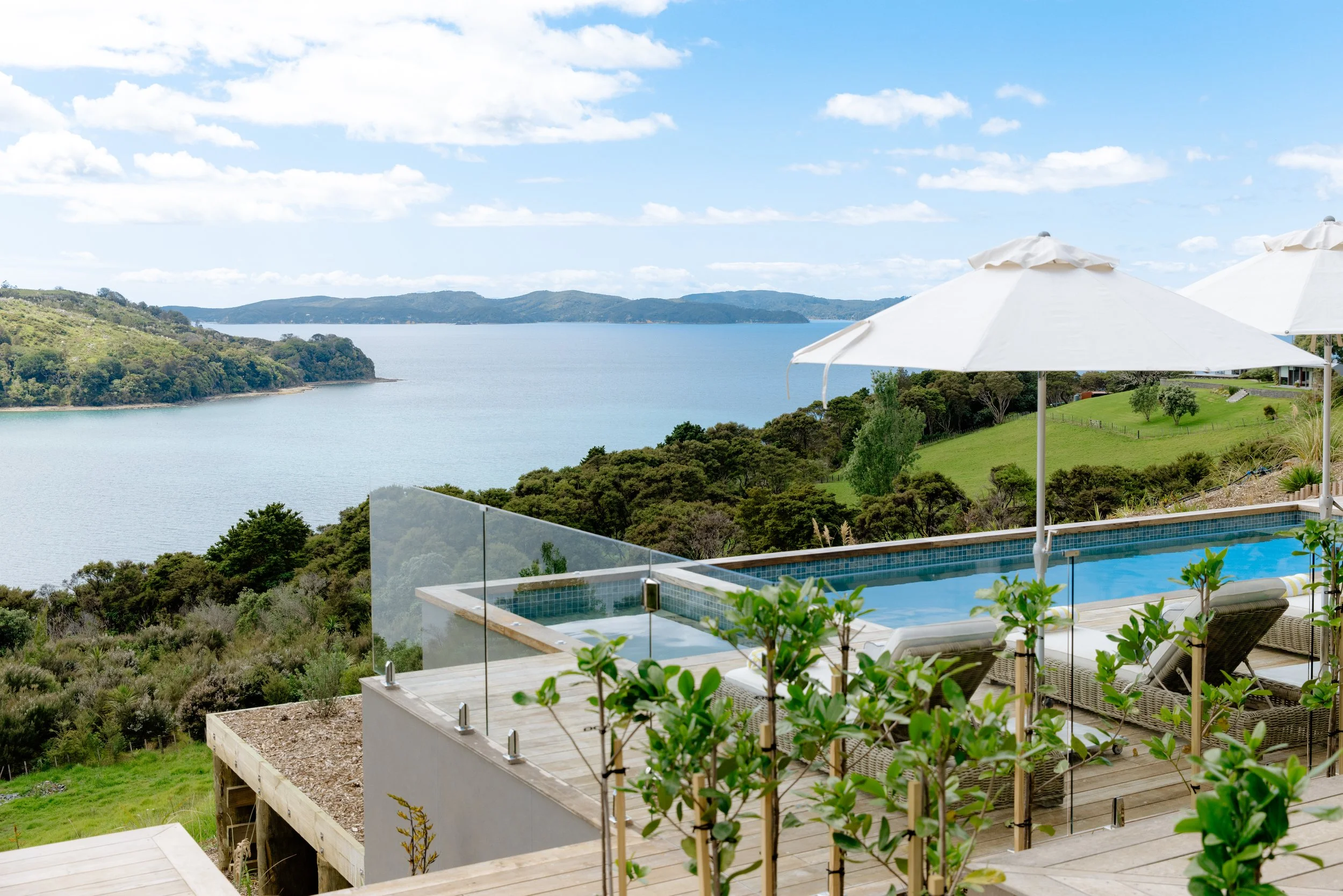 The Farmhouse infinity pool at Bluestone Ridge above native bush, with the Hauraki Gulf and Kawau Island beyond.
