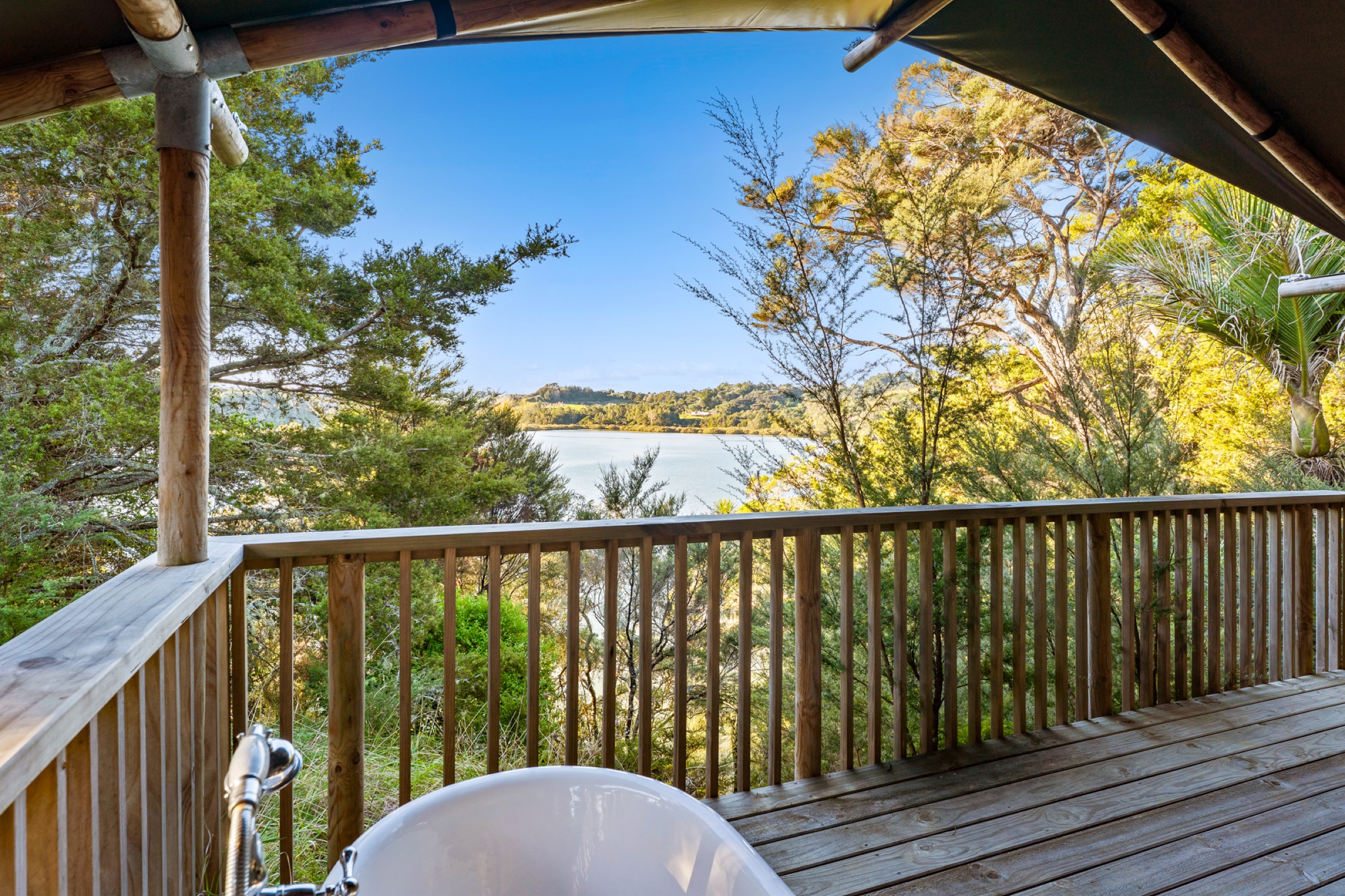 The deck of Safari Tent 1 at Bluestone Encampment: the outdoor bath under the canvas awning, timber balustrade, and the view through the trees to the estuary.